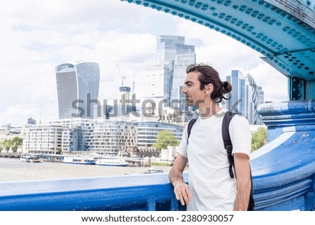 London, UK, 21 june 2023: The City of London skyline Bank Canary Wharf central financial districts skyscrapers sunny day River Thames futuristic buildings man white t-shirt portrait backpack tourist