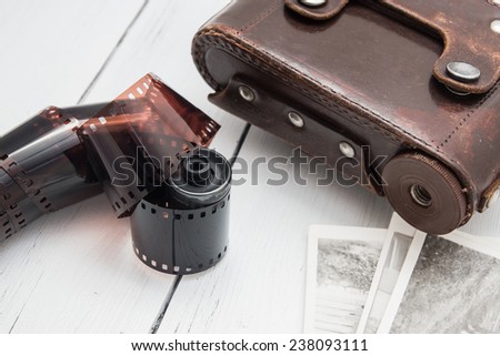 Color film spiral reel  with vintage retro photo case and few printed black and white photos  on a white wooden background