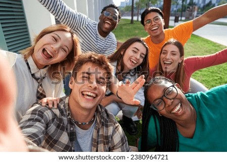 Happy group of multiethnic classmate taking a selfie outdoors in the university campus, looking at camera cheerfully raising arms, celebrating last day. Royalty-Free Stock Photo #2380964721