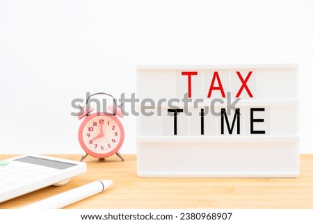 Tax time written white lightbox and calculator with alarm clock on the table.