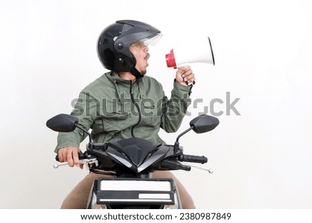 Happy asian man announcing something using megaphone while driving a motorcycle. Isolated on white background Royalty-Free Stock Photo #2380987849