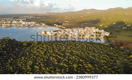 drone aerial view of mediterranean coast at sunrise, port of Porto Colom, typical mediterranean harbour, small fishing port and marina, surrounded by mountains of green mediterranean pines.