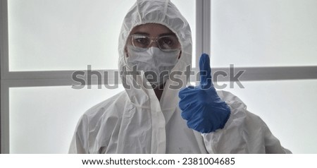 Medical worker or virologist in white protective suit and medical mask shows thumbs up. Doctor makes a recommending gesture ok Royalty-Free Stock Photo #2381004685