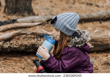 Little girl, child drinks hot tea, water from a thermos to keep warm outdoors in autumn. Photography, portrait.