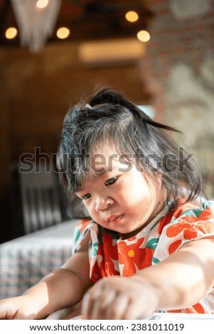 A cute baby girl is using hand to practice eating meal with background of the restaurant. Baby in action photo.