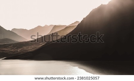 A monochrome landscape photo of a lake in the French Alps, mountain silhouettes created by the backlight of the setting sun, lens flare, cinematic and matte effect, copy space, sepia, 16:9