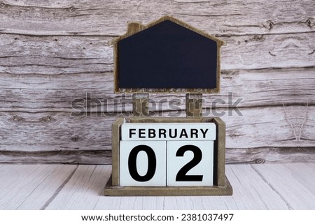 Chalkboard with February 02 calendar date on white cube block on wooden table.