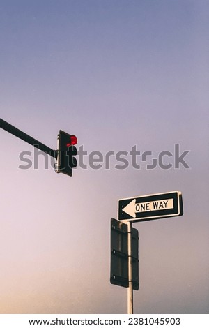 One Way street sign with a clear sky at sunset and a red stoplight