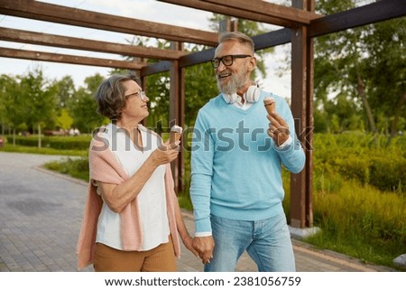 Cheerful senior couple eating ice-cream cone in park enjoying relax time Royalty-Free Stock Photo #2381056759