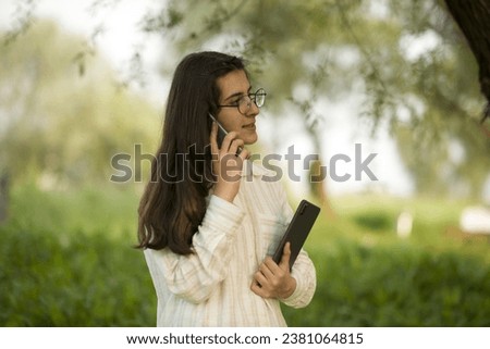 Young business woman having a job interview on the phone, doing business analysis, in the garden of the office, by the lake Royalty-Free Stock Photo #2381064815