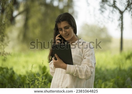 Young business woman having a job interview on the phone, doing business analysis, in the garden of the office, by the lake Royalty-Free Stock Photo #2381064825