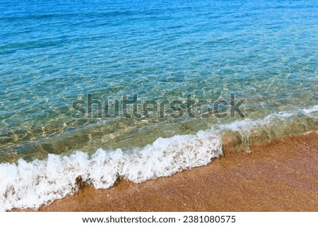 Vivid landscape with sandy beach and blue calm ocean. Small wave on the shore, travel photography. Empty blue sea, picture from the shore.