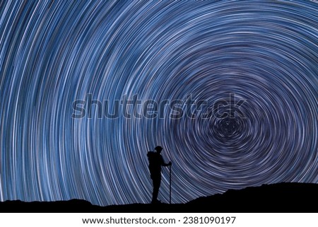 Silhouette of a hiker standing on the hill, on the star trail sky.