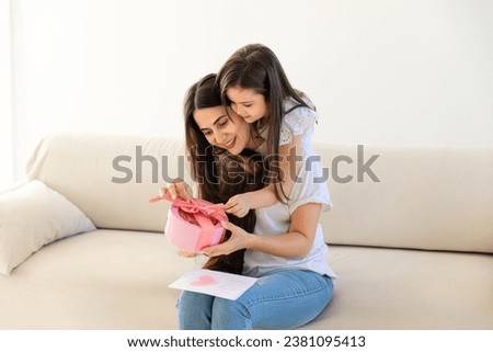 Happy mother's day. Child daughter congratulating her mother and giving her postcard. Mom and girl smiling, kissing and hugging. Family fun and togetherness.