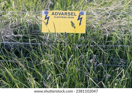 Warning - Electric fence guards a meadow and animals field. Summer season in Denmark Scandinavia.