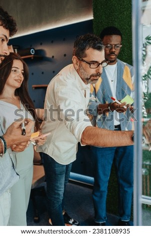 Multiracial colleagues collaborate in a modern office, using sticky notes to share ideas. They discuss strategies and problem-solving, fostering teamwork and innovation for business growth. Royalty-Free Stock Photo #2381108935