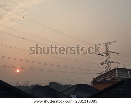 View of the sun in the morning with electric poles and roofs of houses.