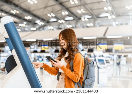 Young Asian woman using self check-in kiosks in airport terminal. Happy and smiley girl online check in by smartphone and getting the boarding pass via machine at international airport Royalty-Free Stock Photo #2381144433