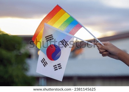 Hand holding rainbow flag and Korean flag which are decorated in homes to show the pride and identity of LGBT people. Soft and selective focus.                              