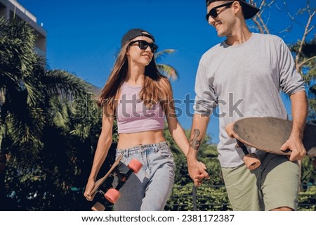 Young happy couple with skateboards enjoy longboarding at the skatepark