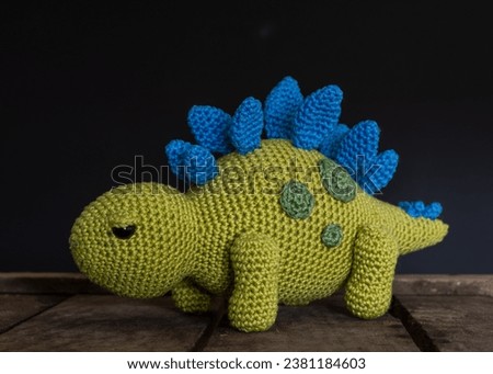 Green and blue stegosaurus on wooden box with black background, toy, handmade, crochet, hobby	