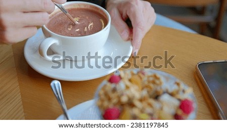Girl hand stirs hot chocolate in white cup with spoon.
