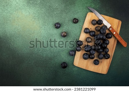 top view of the small sour blue-black fruit sloes on a wooden kitchen board with knife on a green background with copy space
