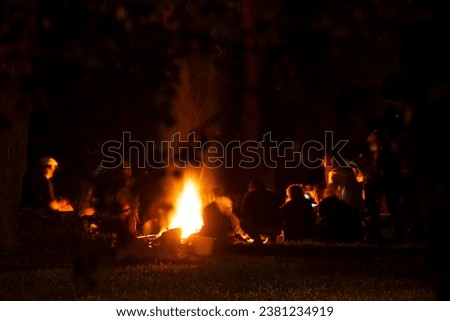 People around a bonfire at night. Figure silhouettes. Unrecognizable. Warm atmosphere.