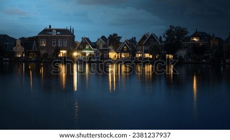 Night shot of houses in Dutch village on riverbank. Lights reflecting on water surface Royalty-Free Stock Photo #2381237937