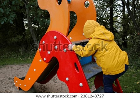 Little caucasian boy climbing on a slide, outdoor playground, early autumn weather  Royalty-Free Stock Photo #2381248727