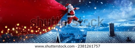 Santa Claus With Red Big Bag Jumping On Roofs In Snowy Winter Landscape - Fast Delivery Present Royalty-Free Stock Photo #2381261757
