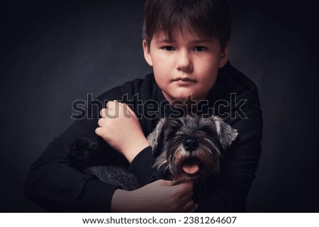 Little boy with a dog on a dark background. Studio shot. Royalty-Free Stock Photo #2381264607