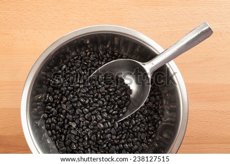Black beans in bowl with transfer scoop on wood table