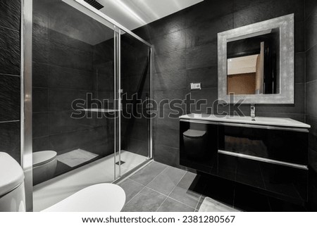 Bathroom all tiled with black slate, glossy black wooden furniture, glass screen Royalty-Free Stock Photo #2381280567