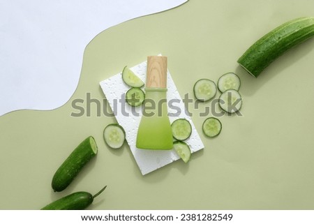 Green plastic bottle with wooden lid placed on a white rectangular podium, fresh cucumbers and cucumber slices decorated around. Simulation scene of homemade cosmetics on pastel background. Royalty-Free Stock Photo #2381282549
