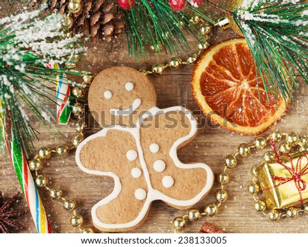 Homemade christmas painted gingerbreads (gingerbread man and red present) on the wooden background with Christmas decorations, cones and candied orange. Selective focus on the man. Toned and snow