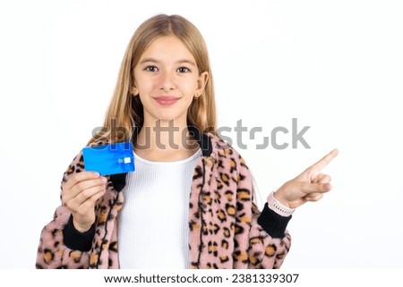 Smiling caucasian kid girl wearing animal print jacket hand showing debit card pointing finger empty space