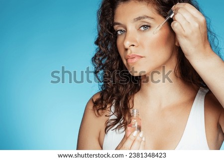 Calm pretty young caucasian woman apply serum to skin, enjoy spa treatments at home, isolated on blue studio background, close up. Wellness, beauty care, healthy lifestyle