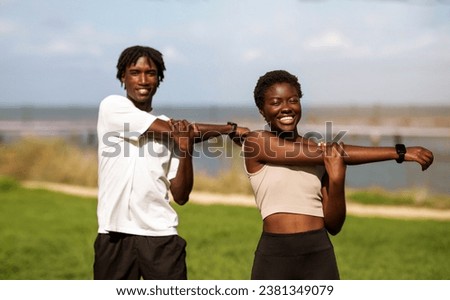 Healthy Lifestyle Concept. Happy black millennial couple training together outdoors, smiling young african american man and woman stretching arm muscles, warming up before jogging outside, copy space