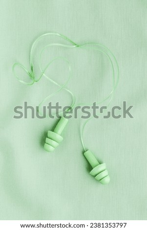 Reusable silicone earplugs green color on colored cloth background, copy space. Soft, flexible ear plug on cord, for swim, sleep, against noise, protect hear, monochrome top view, minimal flat lay