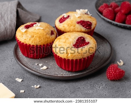 Closeup view of vanilla muffins decorated with heart shaped raspberry. Bright dessert for celebration of saint valentine's day. Grey background. Festive bakery, sweet gift or present for 14 february.  Royalty-Free Stock Photo #2381355107