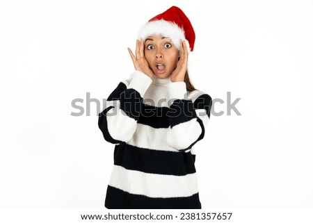 Young beautiful woman wearing striped sweater and a santa claus hat at christmas with scared expression, keeps hands on head, jaw dropped, has terrific expression. Omg concept