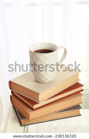 Composition of books with drink cup near sofa on tabletop on the light window background