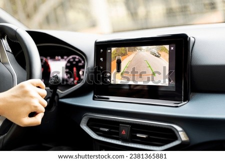 An unrecognizable person is parking a car using the auxiliary parking system using the built-in monitor in the dashboard. Rear view monitor for the car's reversing system. Safety technology equipment. Royalty-Free Stock Photo #2381365881