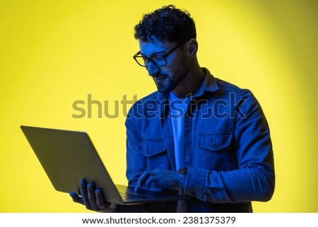 Picture of a pleased young business man posing isolated over light green background wall with led neon lights using laptop computer.