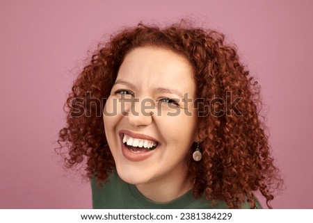Studio headshot of cheerful laughing woman with red curls, demonstrating white teeth, isolated against pink background. Overjoyed young cute female having fun. Dental health, malocclusion