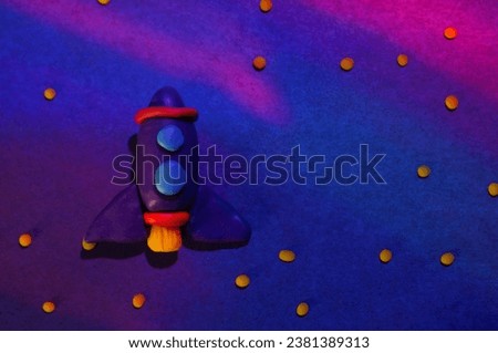 A toy space rocket made of plasticine on a background of colored blue paper.