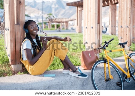 Woman in yellow dungarees sitting outdoors on a sunny day in the city. Cocnepto: lifestyle, outdoors, disconnection Royalty-Free Stock Photo #2381412391