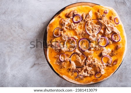 Close up of homemade pizza with canned tuna and red onion on a wooden board top view