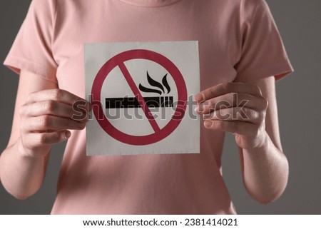 Woman holding card with no smoking sign on gray background, closeup